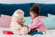 © LIGHTFIELD STUDIOS - Little african american child in pink jacket playing the doctor  with teddy bear