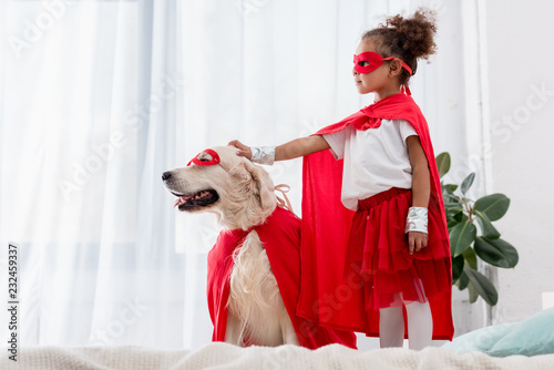 Cuadros en Lienzo Side view of cute little african american kid and dog standing on the bed