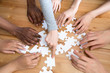 © fizkes - Close up diverse multiracial people hands assembling puzzle scattered on wooden table, top above view. Symbol and metaphor of teamwork and connection, business strategy and logic thinking concept