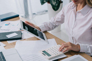 partial view of businesswoman with tablet making calculations at workplace with papers