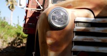 Dropping Down Along The Front Of An Old Rusty Vintage Truck Fender With Glass Headlight And Grill In The Sunlight.