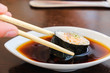 Bowl with tasty soy sauce and chopsticks on white background. Sushi roll with eel. Traditional Japanese food.