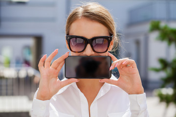 Wall Mural - Young blonde woman showing your smartphone screen, summer park outdoors