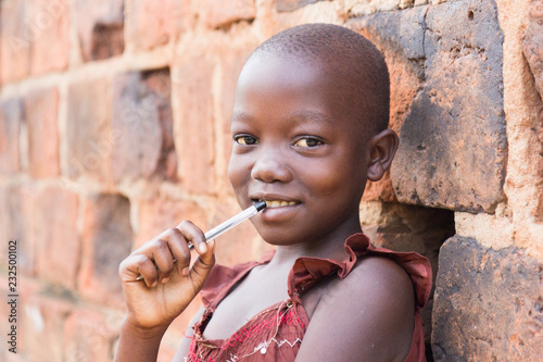 Fotografija An 11-year old Ugandan girl smiling, holding a pen against her mouth and leaning