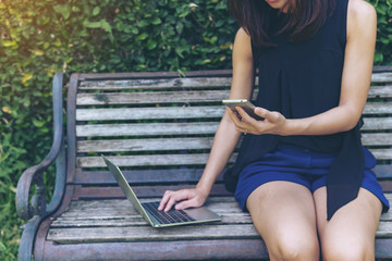 Wall Mural - Close-up of hand woman working using mobile phone and laptop computer outdoor. Technology outdoor concept.