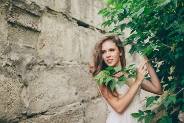 Beautiful happy girl with curly natural hair in white dress near green tree leaves. Summer beauty portrait. Dreamer lady enjoy nature. Inspired woman with dreamy sight in long tunnel in forest.