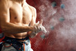 Unrecognizable shirtless male rock climber applying chalk to his hand getting ready to climbing workout against red plastic wall, close up.