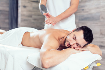 masseur preparing his hands for massage while his clent li lying with closed eyes. close up side view photo