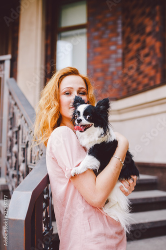 A Beautiful Young Woman With Red Long Hair Is Holding A Small