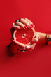 Kobiece eleganckie dłonie. Kobiece dłonie z  czerwonymi paznokciami przez otwór w czerwonym tle  trzymają owoc grejpfruta.