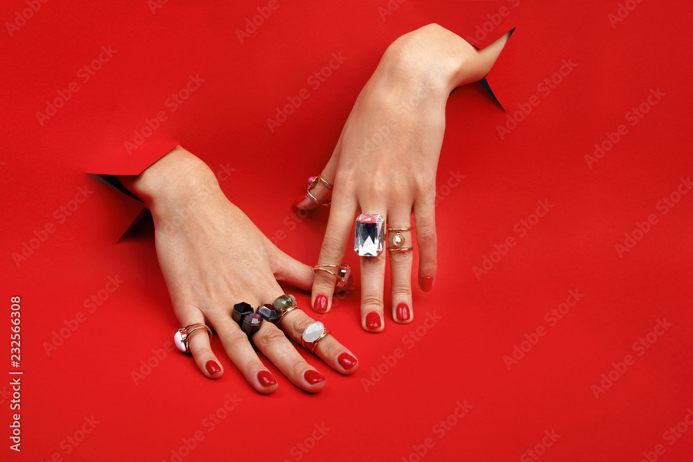Czerwone paznokcie.  Kobiece dłonie na czerwonym tle. Palce z pierścionkami. - obrazy, fototapety, plakaty 