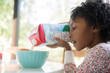 © Stocksy - Girl pouring milk into breakfast cereal