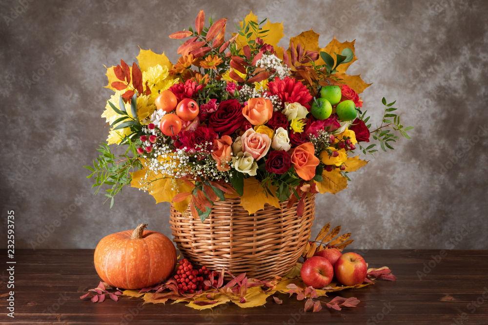 Concept of autumn. Bouquet of beautiful flowers in a basket, pumpkin and yellow leaves - obrazy, fototapety, plakaty 