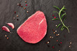 A photo of a steak of eye round beef, a raw cut, with rosemary, garlic, and pepper, shot from above on a black background with a place for text