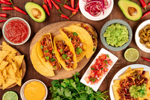 A Photo Of Mexican Food, Including Tacos, Guacamole, Pico De Gallo, Nachos And Others, Shot From The Top With Ingredients On A Dark Rustic Wooden Background