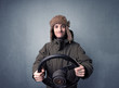 © ra2 studio - Young man holding black steering wheel on a blueish gray background