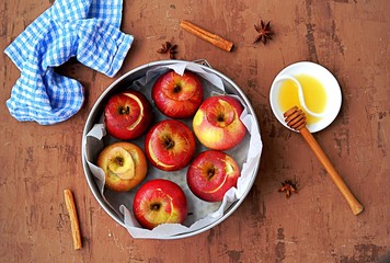 Fresh organic apples prepared for baking, with honey, walnuts and spices in a round baking dish on a brown background. Healthy dessert concept.