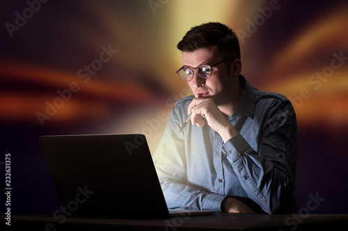 Fotografie, Obraz Young handsome businessman working late at night in the office with warm lights