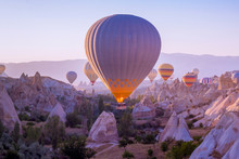 Hot Air Balloons Flying In Beautiful Cappadocia Hilly Landscape, Amazing Tourism Attraction In Goreme, Anatolia, Turkey, Morning Sun Light