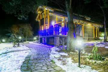 Wall Mural - Winter. The house is decorated for Christmas. New Year. The house is backlit. The cottage is decorated with a garland of light. Winter holidays in the country.