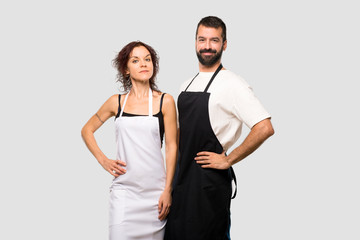 Couple of cooks posing with arms at hip and smiling on grey background