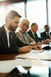 © pressmaster - One of delegates reading text of speech or other document on background of other business people