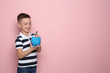 Little boy putting money into piggy bank on color background. Space for text