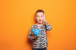 Emotional little boy with piggy bank on color background