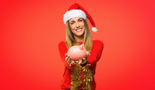 Blonde Woman Dressed Up For Christmas Holidays Taking A Piggy Bank And Happy Because It Is Full On Red Background