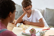 © WHstudio Leushin N - Seious stylish boy in spectacles tries to understand how make task in geometry, listens attentively teacher or tutor, focused into notepad, sits on comfortable couch. Studying and youth concept