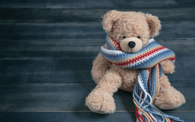 Cute teddy bear with colorful scarf sitting on blue wooden background