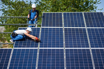 two technicians working with electrical screwdriver connecting shiny solar photo voltaic panel to me