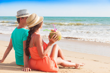 Wall Mural - back view of couple with coconut sitting on a tropical beach in the evening. Khao Lak, Thailand