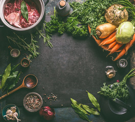 Food background frame with ingredients for tasty Ham Hock Soup : raw beef meat shin with bone, root vegetables, herbs and spices on dark rustic kitchen table with cooking spoon and cast iron pot