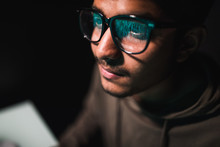 Hacker In Glasses And A Hood Works At A Computer In The Dark, A Reflection In Glasses Close-up.