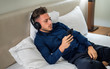 © theartofphoto - Handsome young man in bed listening to music with headphones, using cell phone or MP3 player