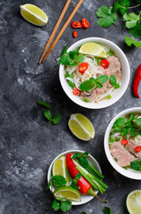 Traditional Vietnamese Soup Pho Bo with Rice Noodles, Beef and Herbs on Dark Background