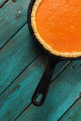 Wall Mural - Bright pumpkin pie in cast iron pan on turquoise background minimalist style