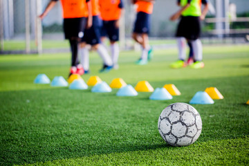 Wall Mural - Soccer ball on green artificial turf with blurry of maker cones and player training.