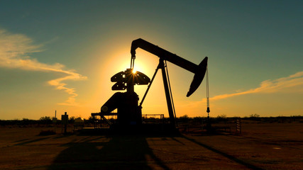 Industrial jack pump platform pumping crude oil over sunset sun