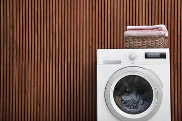 Wall Mural - Washing machine and laundry basket with towels near wooden wall. Space for text