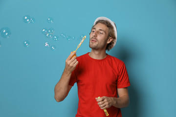 Young man blowing soap bubbles on color background