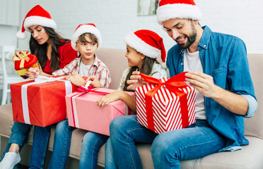 Wall Mural - Big happy and cheerful family in santa hats giving christmas presents in living room while New Year holidays