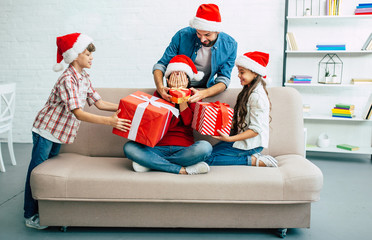 Wall Mural - Presents for lovely mother. Joyful and happy family in santa hats giving christmas presents in living room while New Year holidays