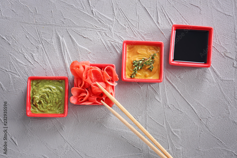 Different tasty sauces with marinated ginger in bowls on grey background