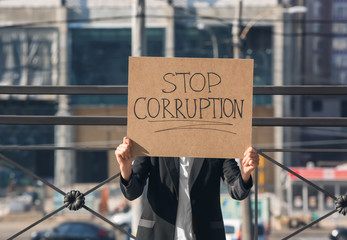 Woman holding placard with text STOP CORRUPTION outdoors