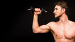 © Stavros - Confident young man shirtless portrait training with dumb-bell against black background.