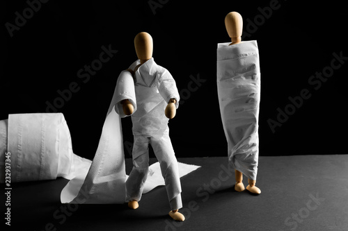 Cuadros en Lienzo Funny wooden mannequins wrapped in toilet paper on table against dark background