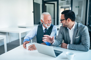 Smiling senior and junior business men at work.