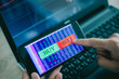 © chompoo - Hand of trader holding mobile phone touch screen showing buy and sell in Stock market order and blurred bakcground of laptop show financial chart, business trading concept